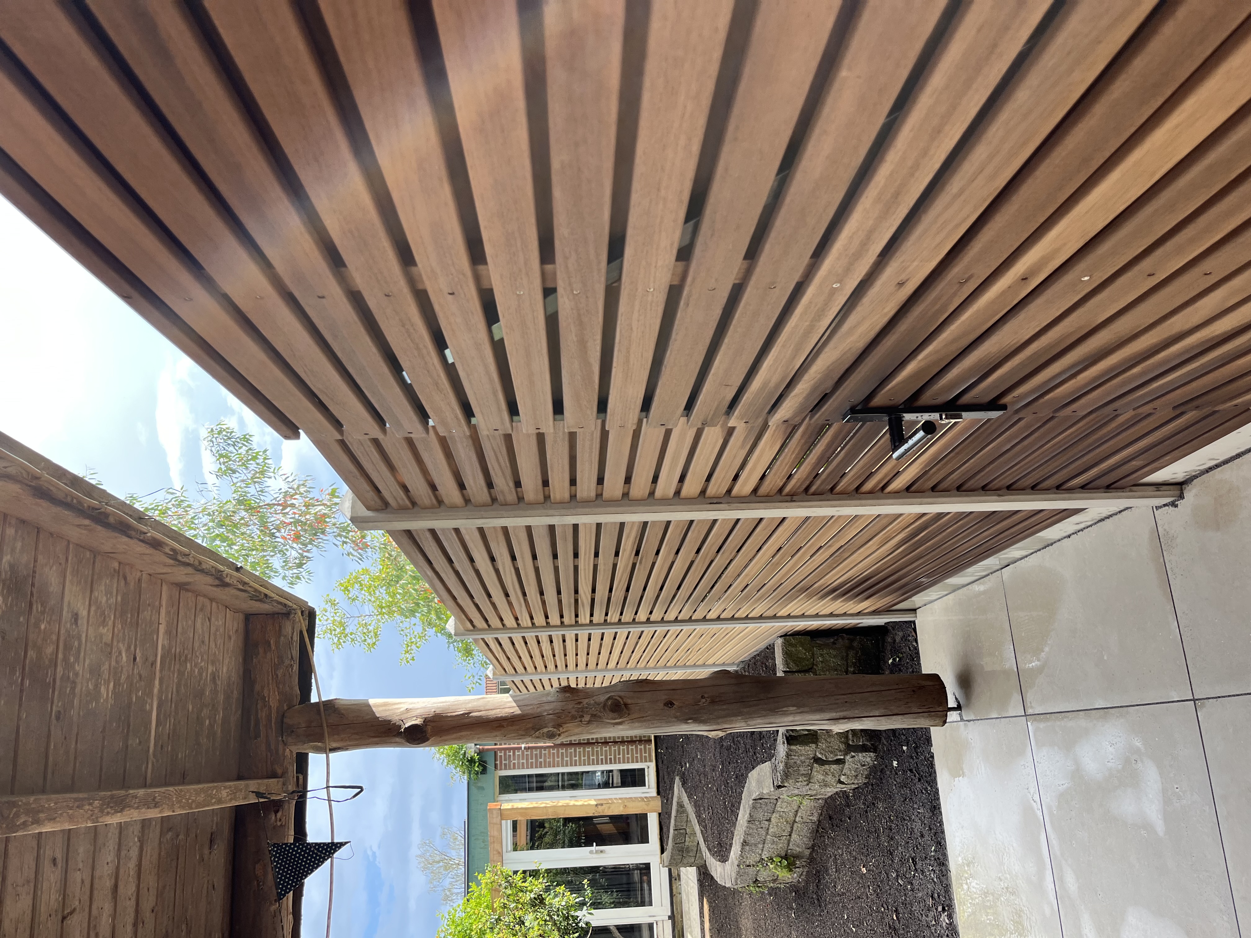 Detail houten pergola met lamellen en sfeerverlichting — Westhuis Tuinen